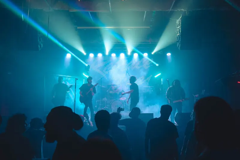 The band on stage seen from the back of a full room, light beams over the crowd