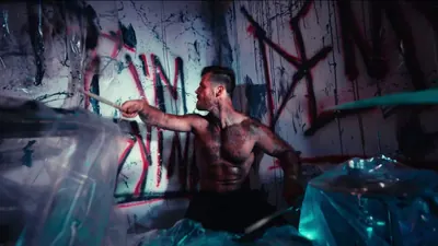 Video still: the drummer playing in a room wrapped in plastic, walls covered in red graffiti